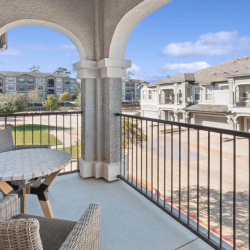 a patio with a table and chairs on a deck with buildings in the background